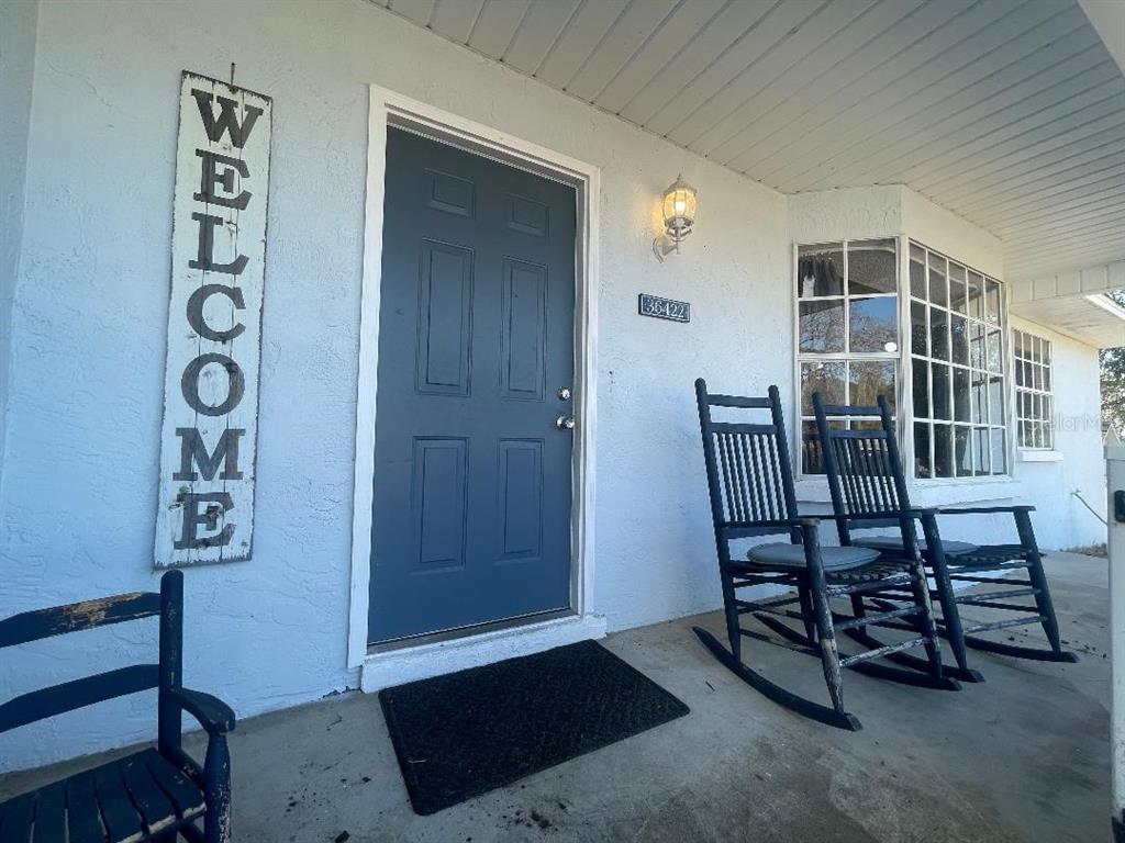 A front porch features a blue door, a welcome sign, and two black rocking chairs — 36422 BIRDIE COURT, GRAND ISLAND, FL