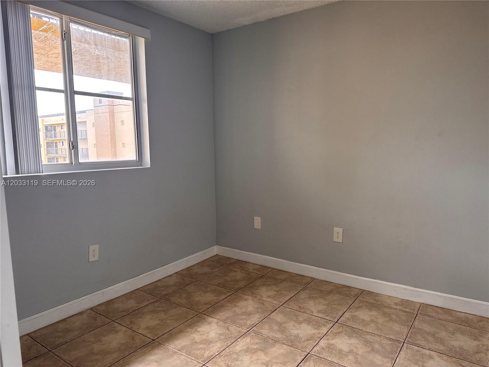 An empty room features light gray walls, tile flooring, and a single window — 14931 SW 82nd Ln # 403, Miami FL 33193, MIAMI, FL