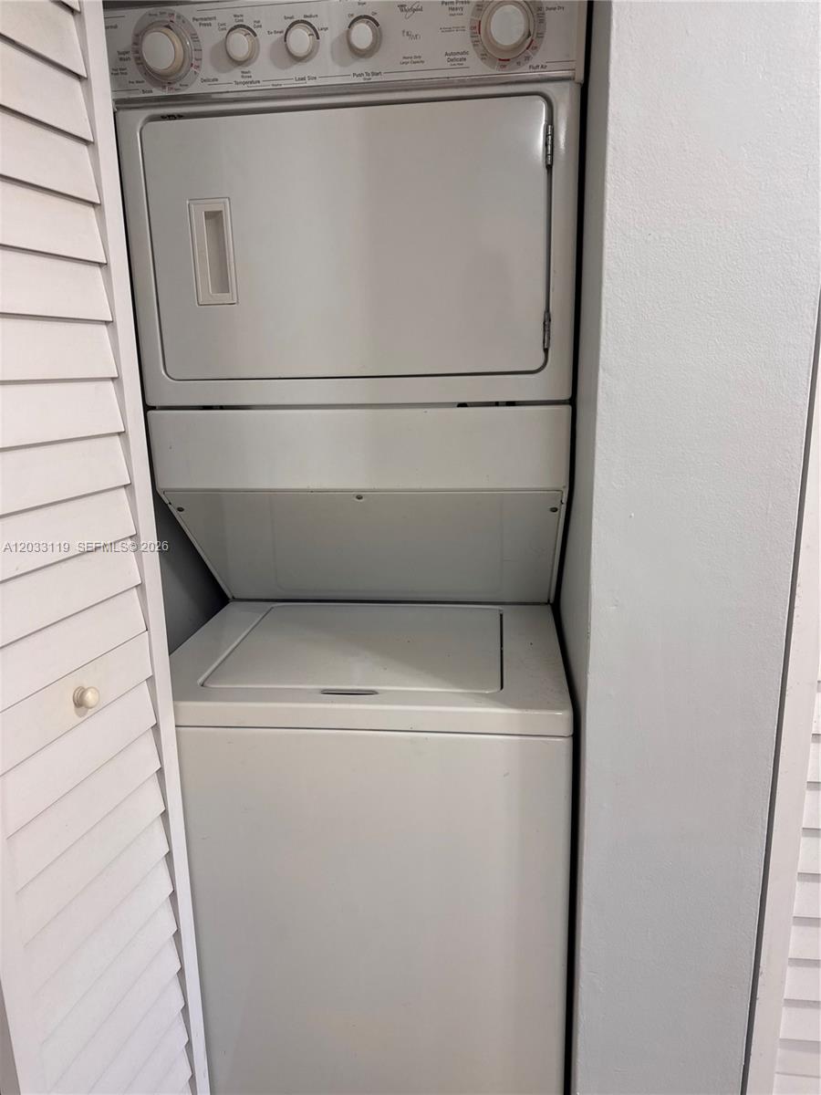A white stacked washer and dryer unit is installed in a small laundry closet — 14931 SW 82nd Ln # 403, Miami FL 33193, MIAMI, FL