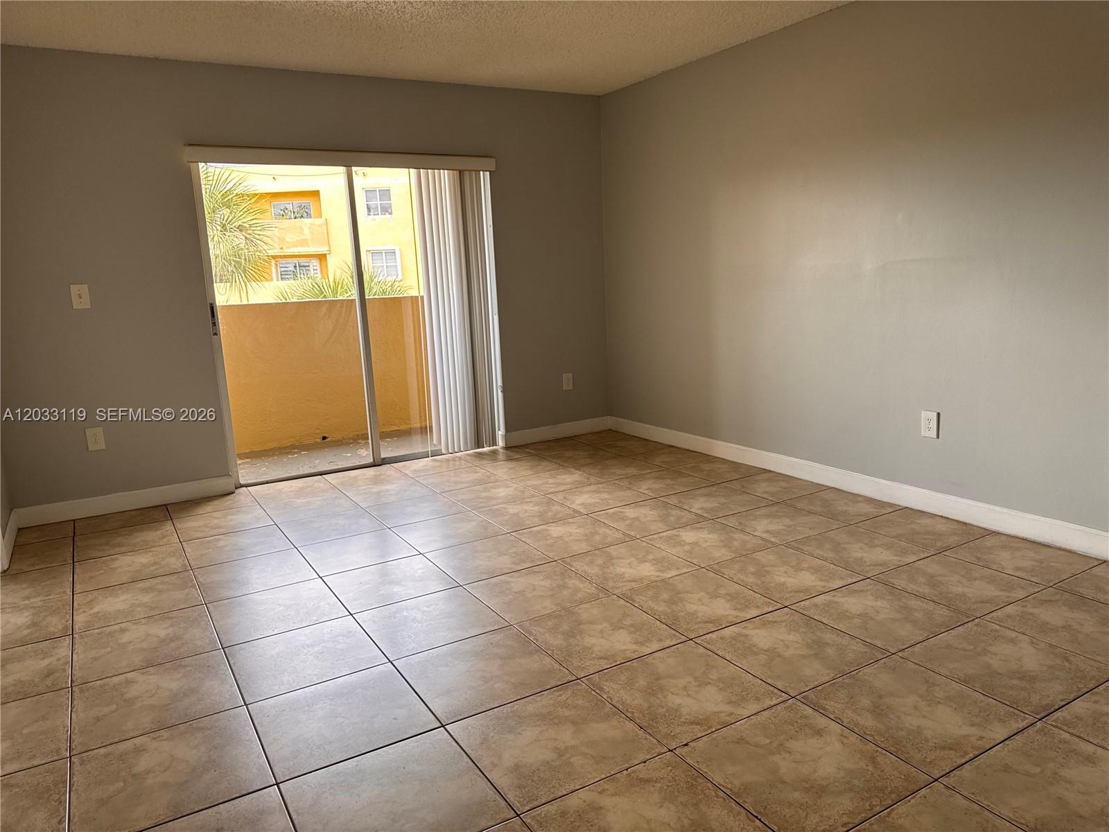 An empty room features light gray walls, tan tile flooring, and a sliding glass door — 14931 SW 82nd Ln # 403, Miami FL 33193, MIAMI, FL