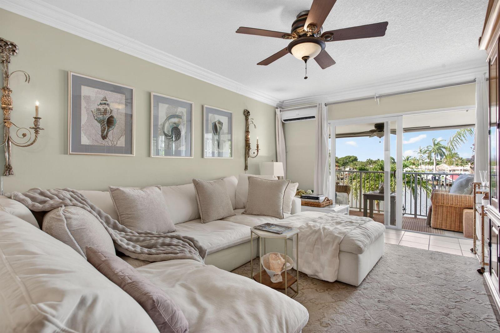 A living room features a white sectional sofa, shell artwork, and a balcony overlooking water — 800 Pine Drive # 13, Pompano Beach FL 33060, POMPANO BEACH, FL
