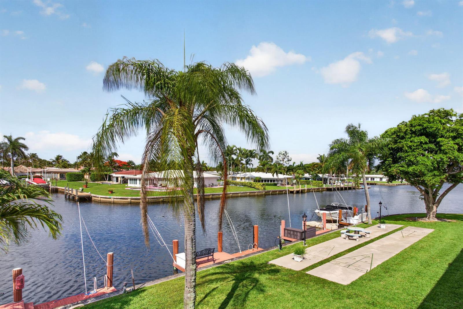 A waterfront view featuring a canal, boat docks, a palm tree, and a shuffleboard court — 800 Pine Drive # 13, Pompano Beach FL 33060, POMPANO BEACH, FL