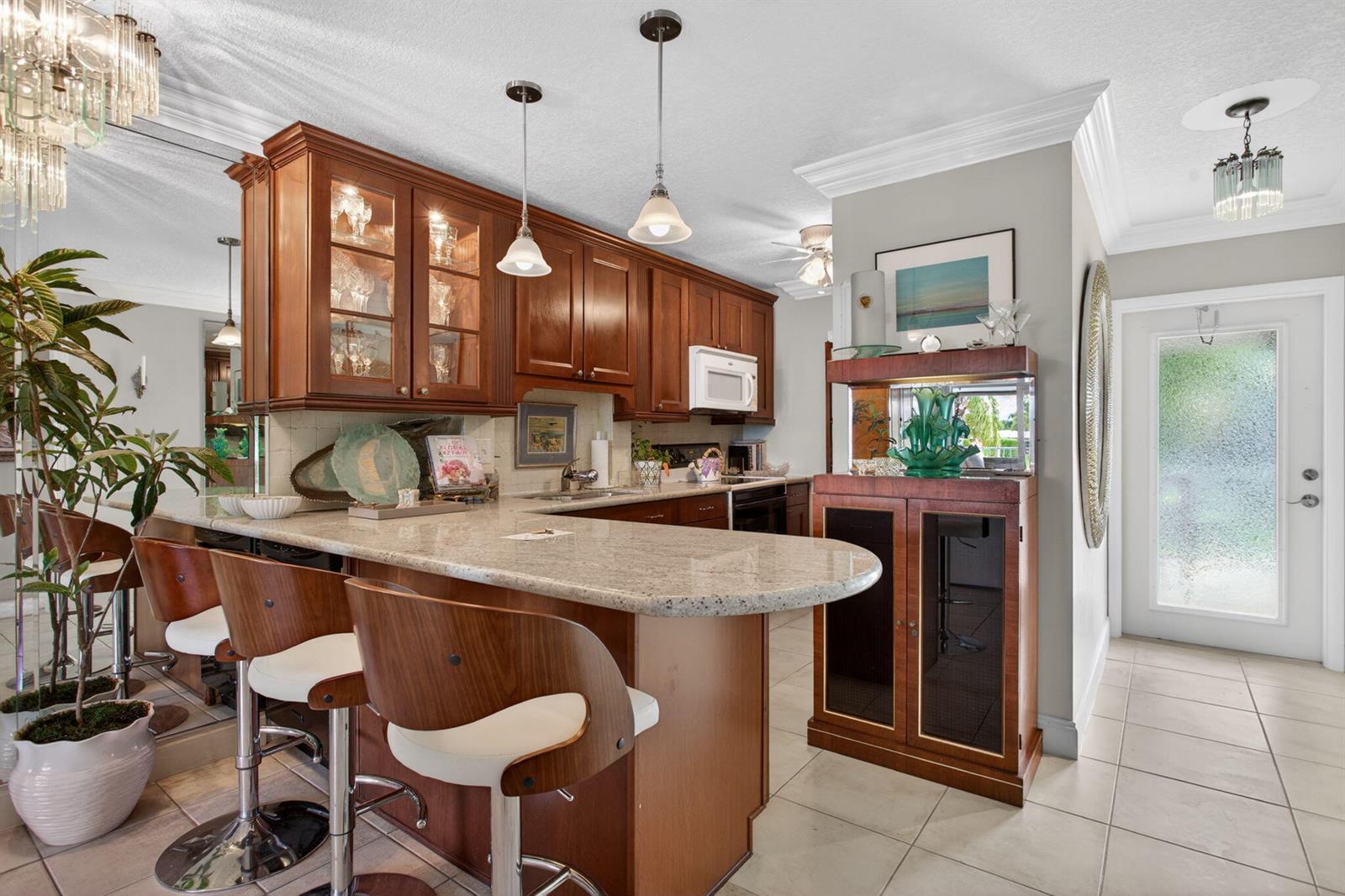 A kitchen features wood cabinets, granite countertops, a breakfast bar with stools, and tile flooring — 800 Pine Drive # 13, Pompano Beach FL 33060, POMPANO BEACH, FL