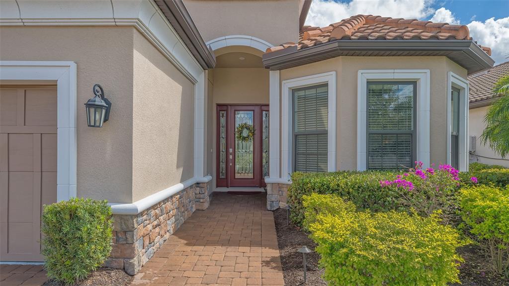 A paved walkway leads to the front entrance of a house with stone accents — 4719 CASSIO COURT, BRADENTON, FL