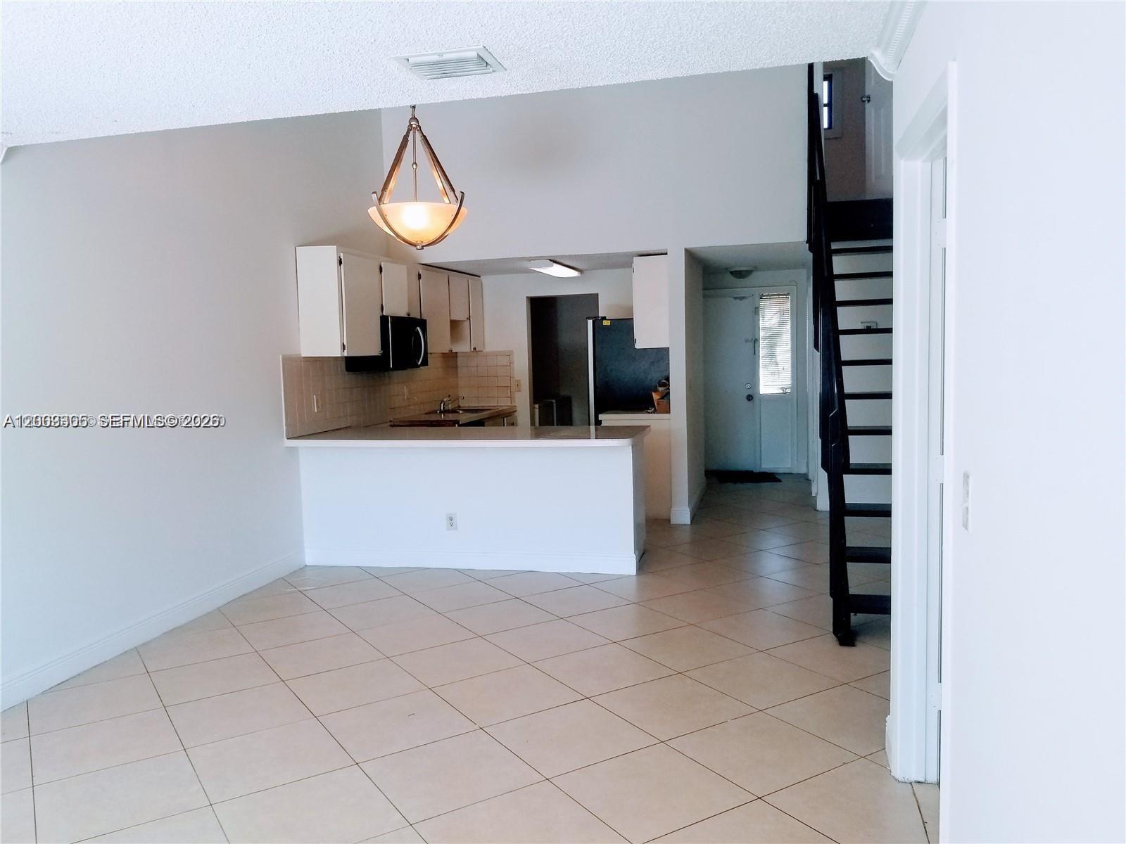 An open-concept kitchen with white cabinets and a breakfast bar overlooks a tiled living area — 6943 SW 40th St # R, Miramar FL 33023, MIRAMAR, FL