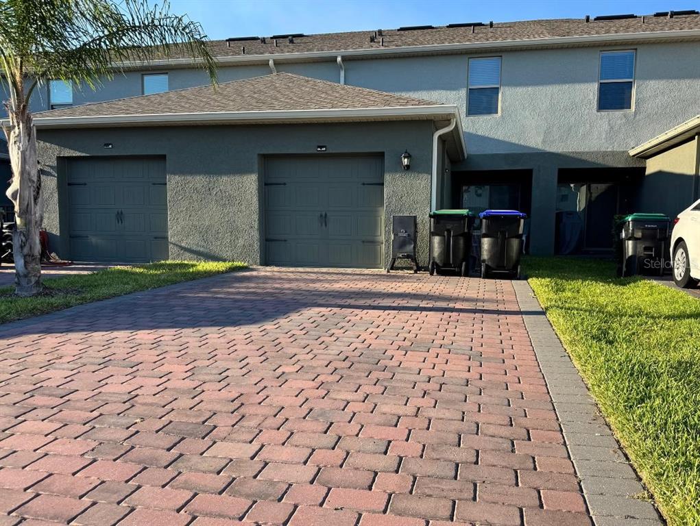 A two-car garage with a brick paver driveway and trash bins in front of townhomes — 13286 PONTOON RD, WINTER GARDEN, FL