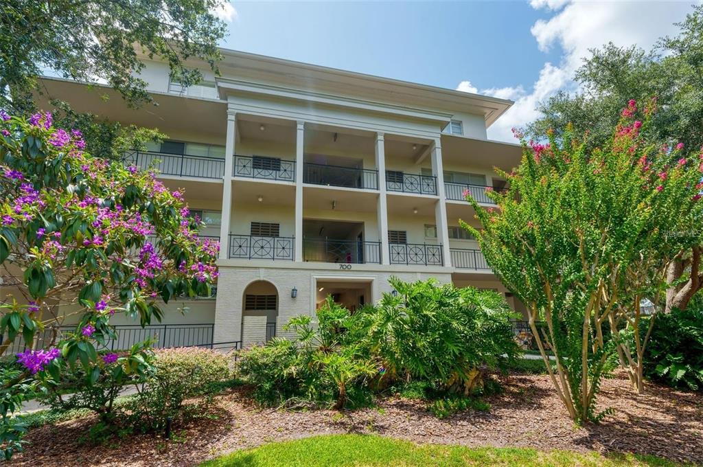 A three-story apartment building with balconies and a central entrance surrounded by landscaping — 700 MELROSE AVENUE UNIT J24, WINTER PARK, FL