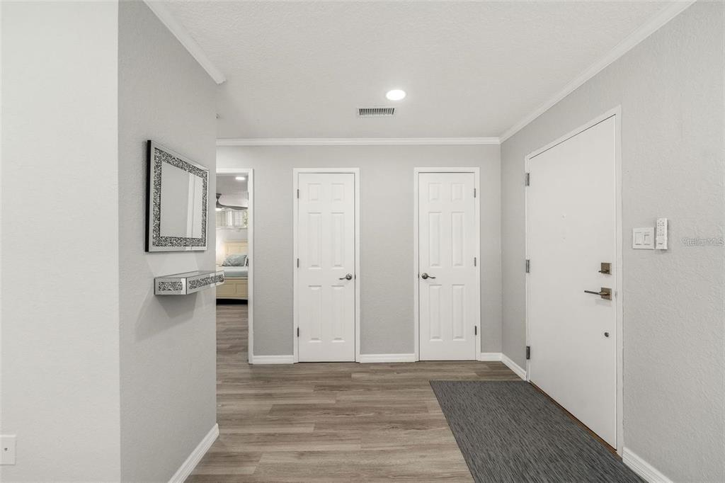 An entryway with grey wood-look flooring, two white doors, and a white front door — 700 MELROSE AVENUE UNIT J24, WINTER PARK, FL