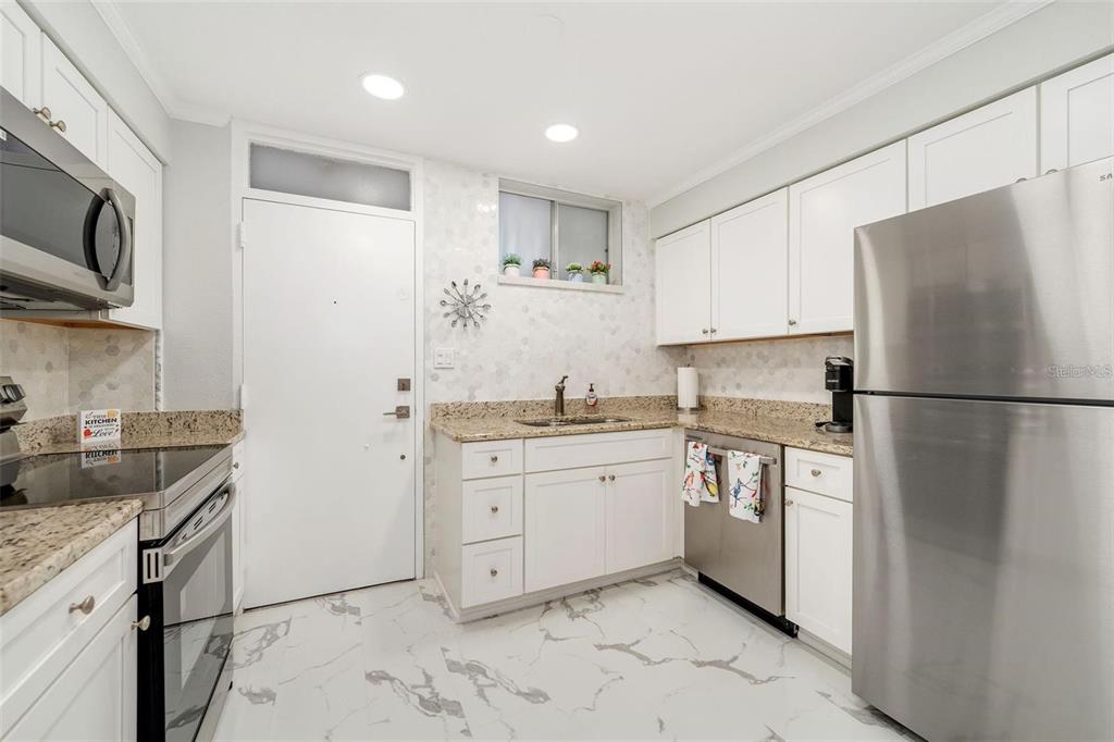 A kitchen with white cabinets, stainless steel appliances, granite countertops, and white marble-patterned tile flooring — 700 MELROSE AVENUE UNIT J24, WINTER PARK, FL