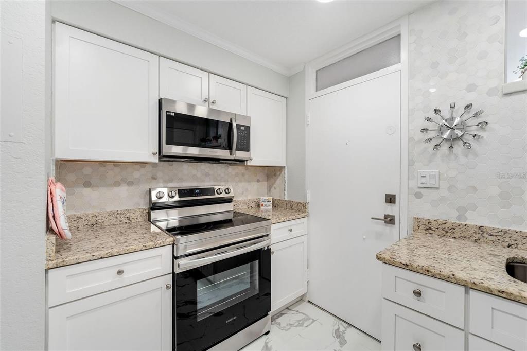 A kitchen features white cabinets, granite countertops, stainless steel appliances, and a hexagonal tile backsplash — 700 MELROSE AVENUE UNIT J24, WINTER PARK, FL