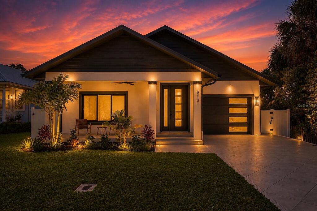A modern single-story house with a dark roof, white exterior, and an attached garage at sunset — 813 E 1ST AVENUE, NEW SMYRNA BEACH, FL