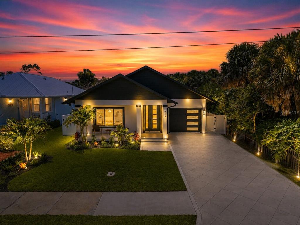 A modern single-story house with a paved driveway and illuminated exterior at sunset — 813 E 1ST AVENUE, NEW SMYRNA BEACH, FL