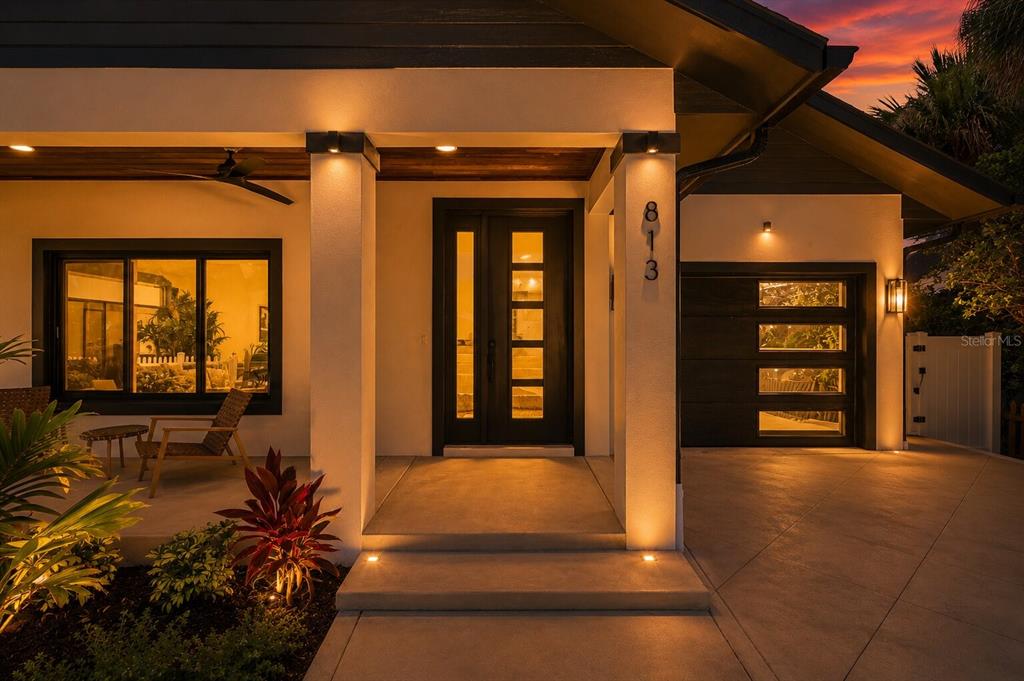 A modern house exterior features a dark front door, a garage, and warm porch lighting — 813 E 1ST AVENUE, NEW SMYRNA BEACH, FL
