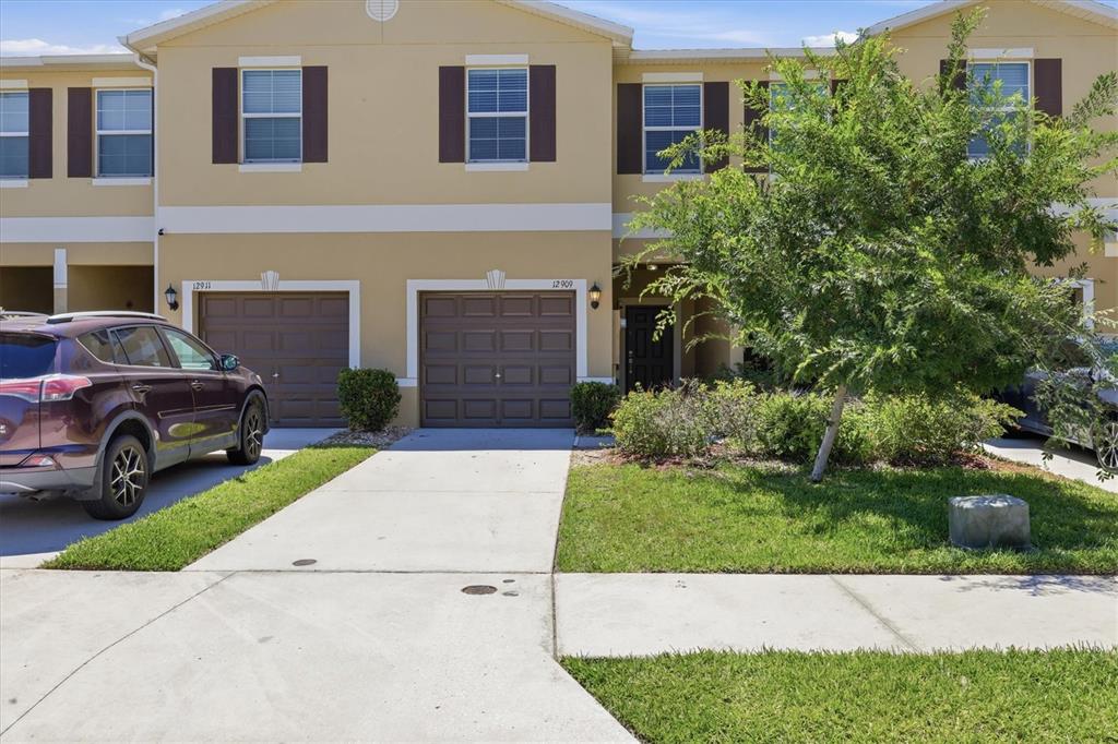 A two-story townhouse exterior features a beige facade, two garage doors, and a front lawn — 12909 DREAM CATCHER WAY, RIVERVIEW, FL