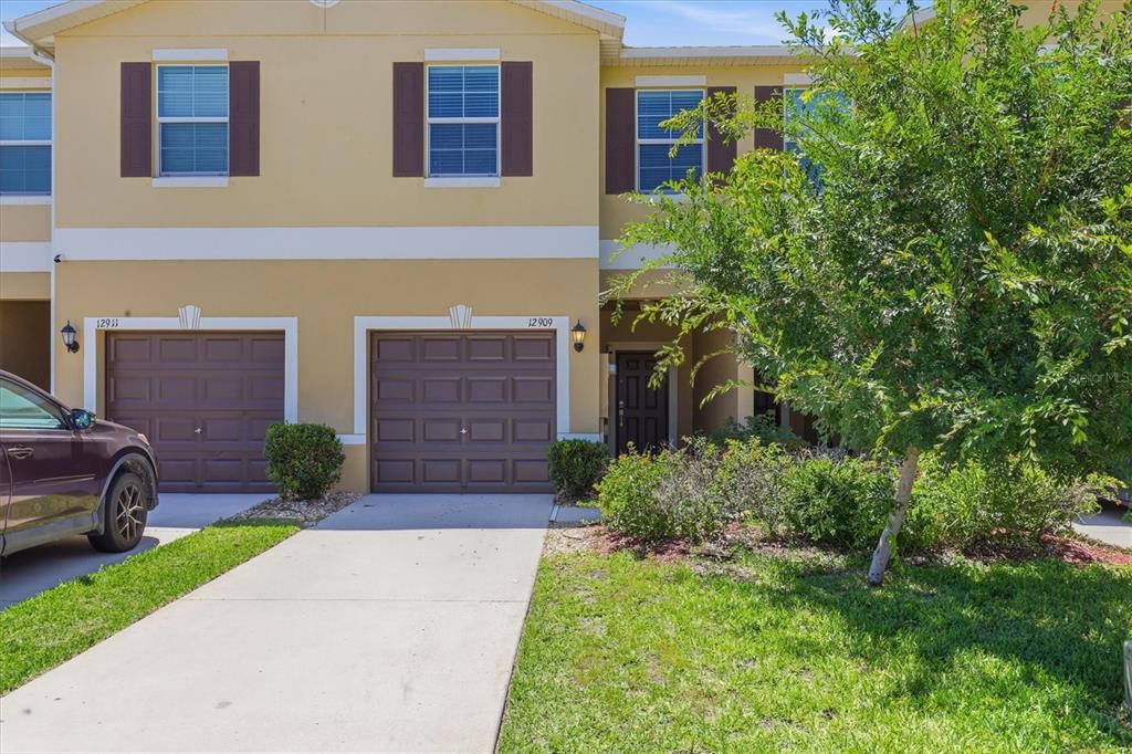 A two-story townhouse exterior features tan stucco walls, brown garage doors, and a concrete driveway — 12909 DREAM CATCHER WAY, RIVERVIEW, FL