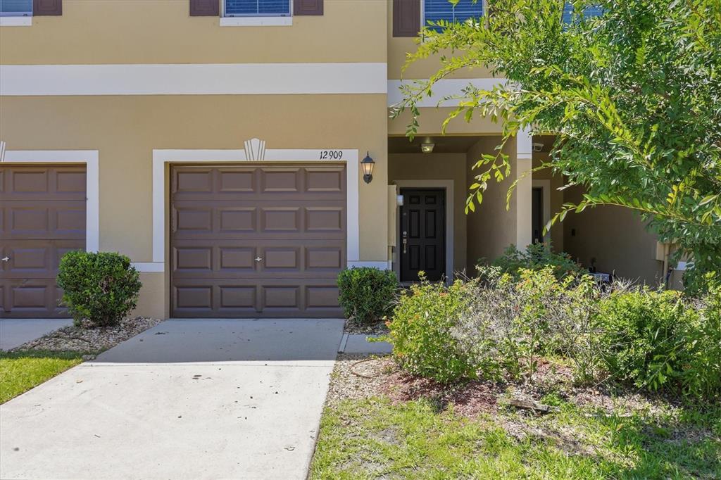 A tan townhouse exterior features a brown garage door, a front entrance, and landscaping — 12909 DREAM CATCHER WAY, RIVERVIEW, FL