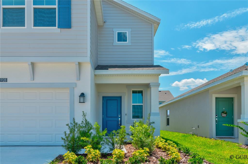 A two-story house exterior features a blue front door, light siding, and a garage — 1928 ROCK MAPLE BEND, KISSIMMEE, FL
