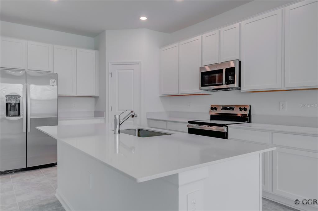 A modern kitchen features white cabinetry, a central island with a sink, and stainless appliances — 1928 ROCK MAPLE BEND, KISSIMMEE, FL