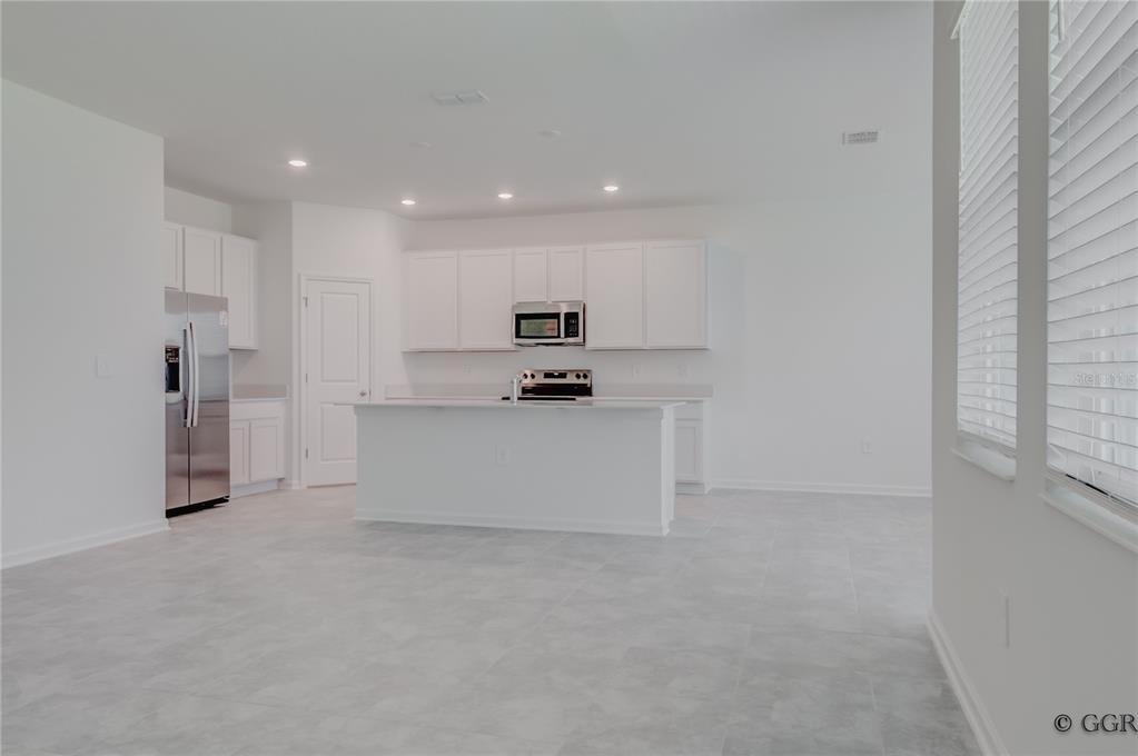 A modern kitchen features white cabinets, stainless steel appliances, a center island, and tile flooring — 1928 ROCK MAPLE BEND, KISSIMMEE, FL