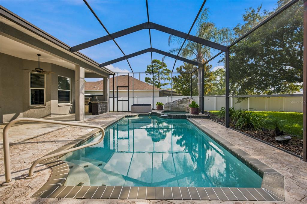 A screened-in patio features a swimming pool with a spa and an outdoor kitchen area — 5517 GREYSTONE DRIVE, SPRING HILL, FL
