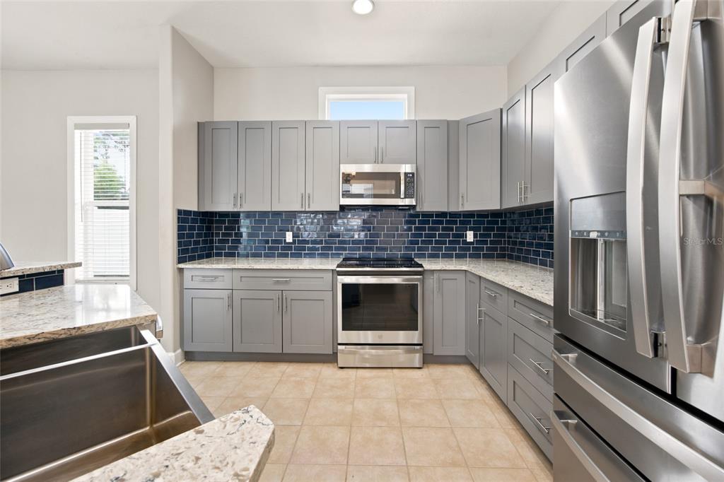 A kitchen features gray cabinets, a blue subway tile backsplash, and stainless steel appliances — 5517 GREYSTONE DRIVE, SPRING HILL, FL