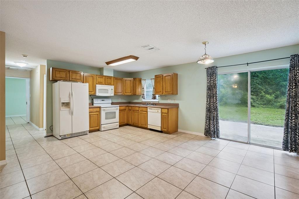 A kitchen with light wood cabinets, white appliances, tile flooring, and a sliding glass door — 1531 19TH STREET, ORANGE CITY, FL