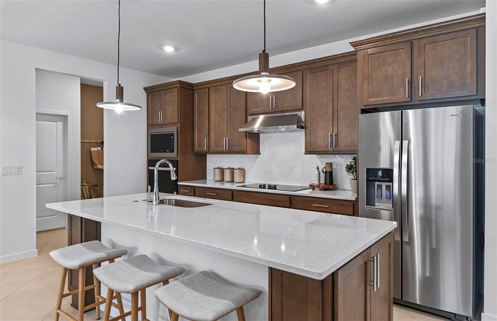 A modern kitchen features dark wood cabinets, a white quartz island, and stainless steel appliances — 8169 SW 44TH COURT ROAD, OCALA, FL