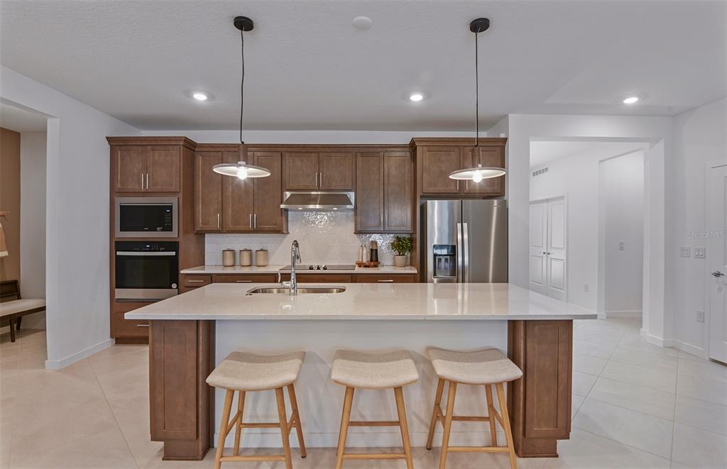 A modern kitchen features wood cabinets, a large quartz island with stools, and stainless appliances — 8169 SW 44TH COURT ROAD, OCALA, FL