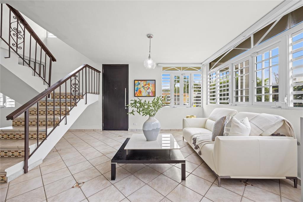 A living room features tiled floors, a staircase with iron railings, and a white sofa — Calle 6 H17 TINTILLO GARDENS, GUAYNABO, PR