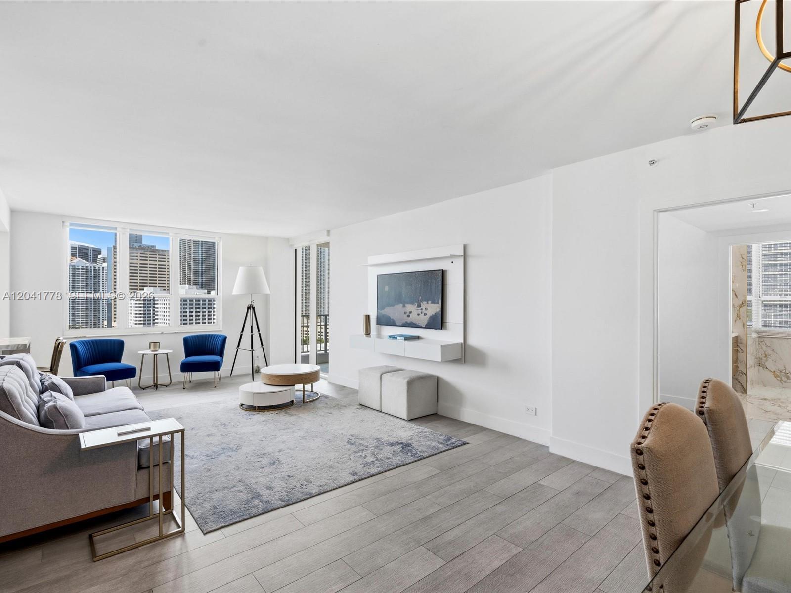 A bright living room features a grey sofa, blue accent chairs, and city skyline views — 701 Brickell Key Blvd # 1903, Miami FL 33131, MIAMI, FL