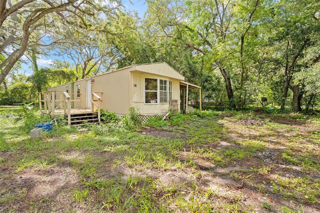 A single-story mobile home with a wooden deck sits on a wooded, grassy lot — 122 ARKAYS AVENUE, SPRING HILL, FL