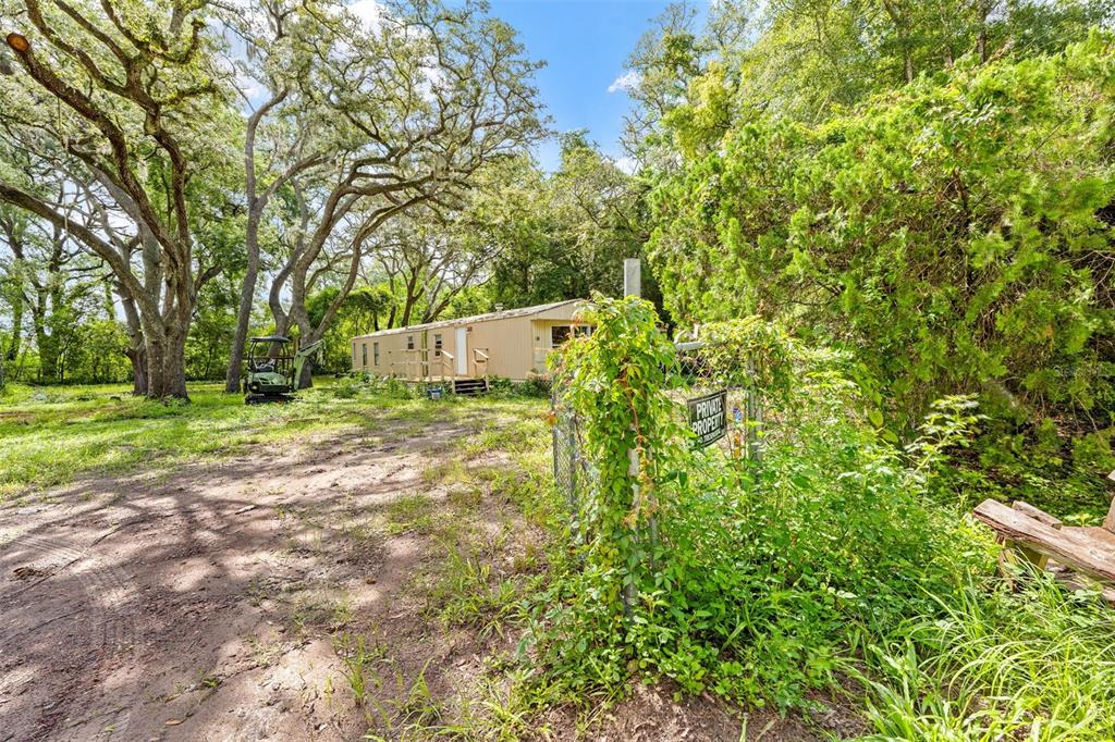 A mobile home sits on a dirt lot surrounded by trees and a chain-link fence — 122 ARKAYS AVENUE, SPRING HILL, FL
