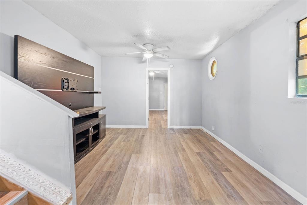 A living room features light wood-look flooring, gray walls, and a dark wood media console — 122 ARKAYS AVENUE, SPRING HILL, FL