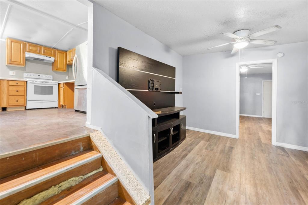 A living room with wood-look flooring leads to a kitchen with wood cabinets and stairs — 122 ARKAYS AVENUE, SPRING HILL, FL