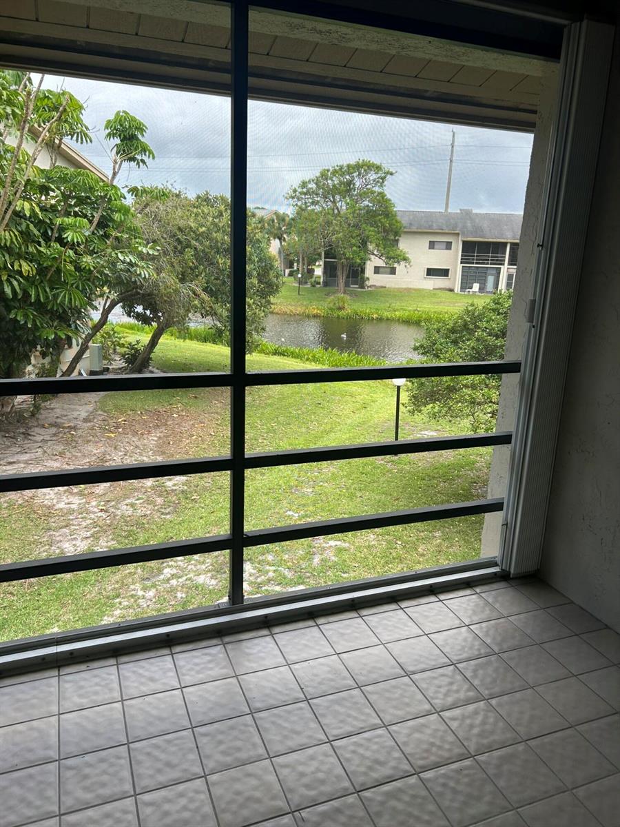 A tiled balcony with a screen enclosure overlooks a grassy lawn, pond, and apartment buildings — 3001 SE Aster Lane # 908, Stuart FL 34994, STUART, FL