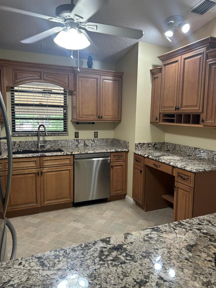 A kitchen features wood cabinets, granite countertops, a stainless steel dishwasher, and a ceiling fan — 3001 SE Aster Lane # 908, Stuart FL 34994, STUART, FL