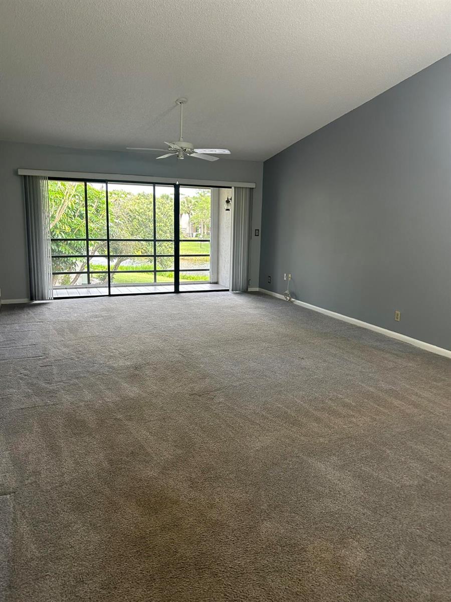 An empty living room features gray walls, beige carpeting, and a sliding glass door — 3001 SE Aster Lane # 908, Stuart FL 34994, STUART, FL