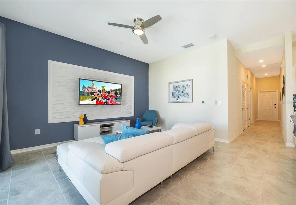 A living room features a white sectional sofa, a wall-mounted television, and tiled flooring — 3180 PARADOX CIRCLE UNIT 405, KISSIMMEE, FL