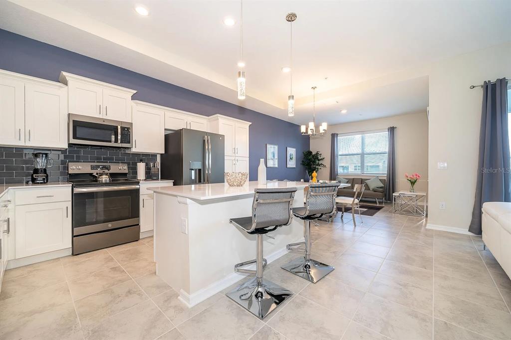 A modern kitchen features white cabinets, stainless steel appliances, a center island, and blue walls — 3180 PARADOX CIRCLE UNIT 405, KISSIMMEE, FL
