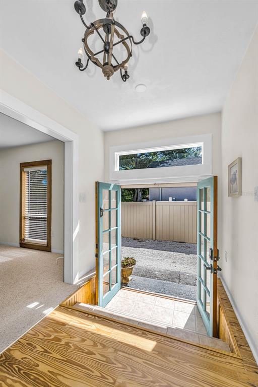 An entryway features a chandelier, light-colored walls, wood flooring, and double doors opening outdoors — 525 BAY STREET, DUNEDIN, FL