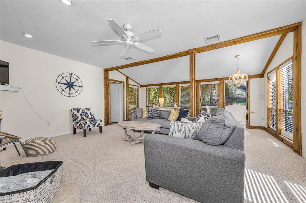 A living room features carpeted floors, a ceiling fan, and large windows with wooden trim — 525 BAY STREET, DUNEDIN, FL