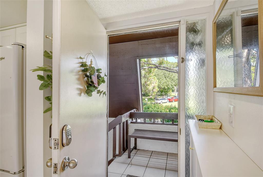 An open front door reveals a small tiled balcony with a bench and outdoor view — 4616 RINGWOOD MEADOW UNIT 20, SARASOTA, FL