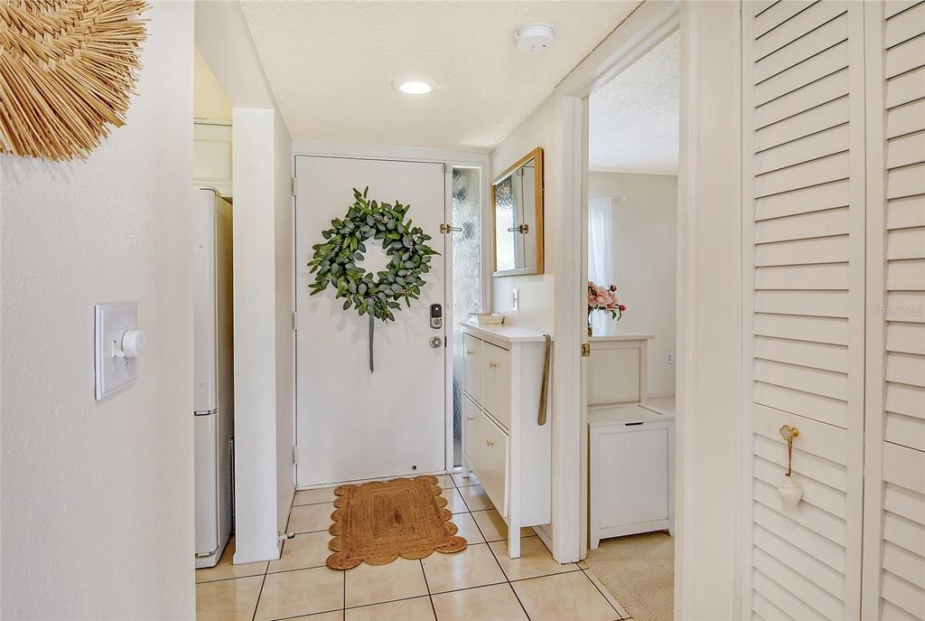 A bright entryway features tiled floors, a white door with a wreath, and a shoe cabinet — 4616 RINGWOOD MEADOW UNIT 20, SARASOTA, FL