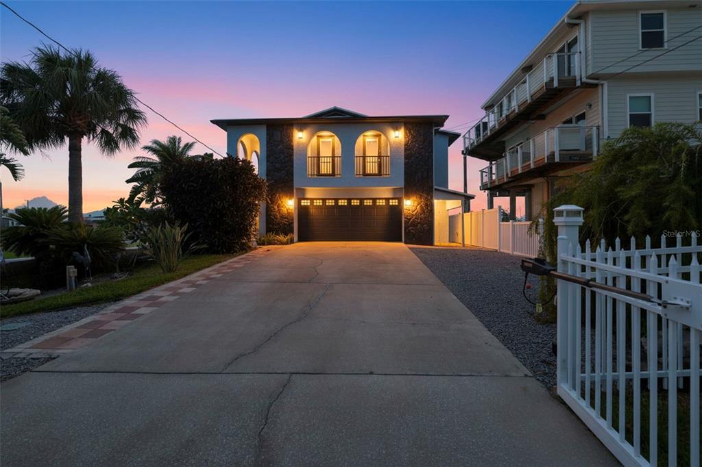 A two-story house with a large garage, arched balconies, and a concrete driveway at sunset — 3420 EAGLE NEST DRIVE, HERNANDO BEACH, FL