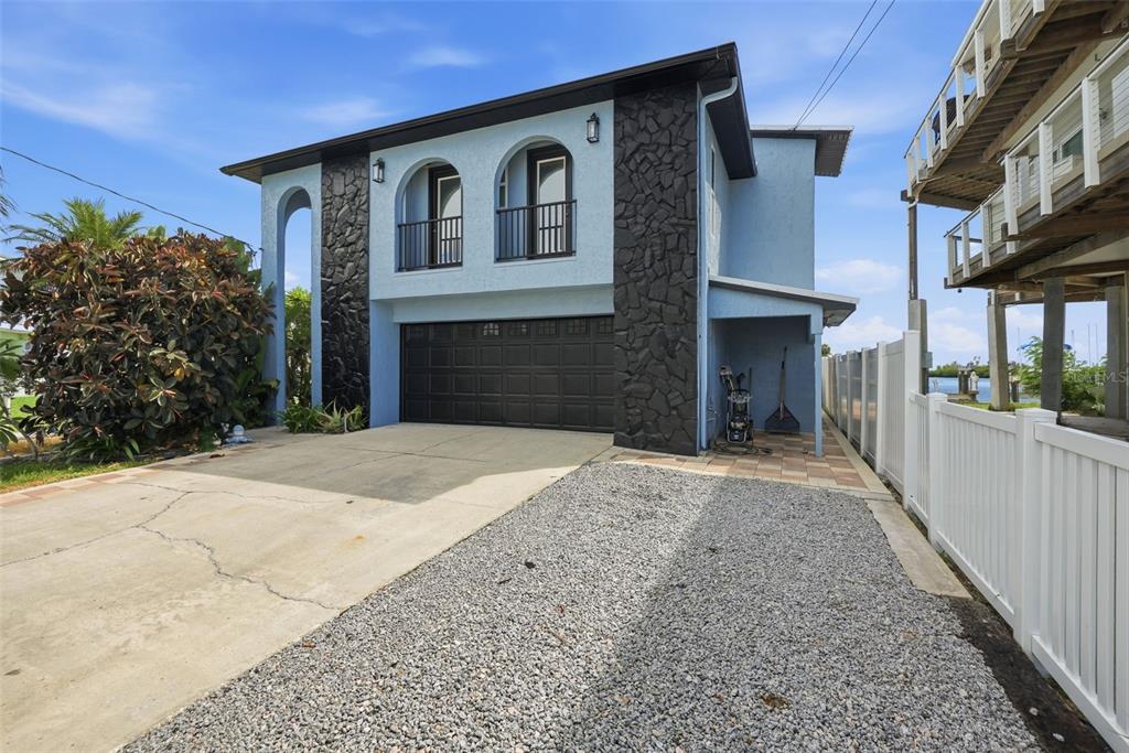 A two-story blue house with black stone accents, a garage, and a gravel driveway — 3420 EAGLE NEST DRIVE, HERNANDO BEACH, FL