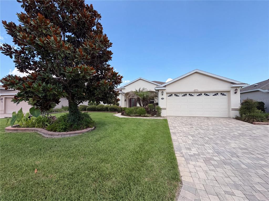 A single-story house features a paved driveway, a two-car garage, and a large magnolia tree — 27103 CAMERONS RUN, LEESBURG, FL