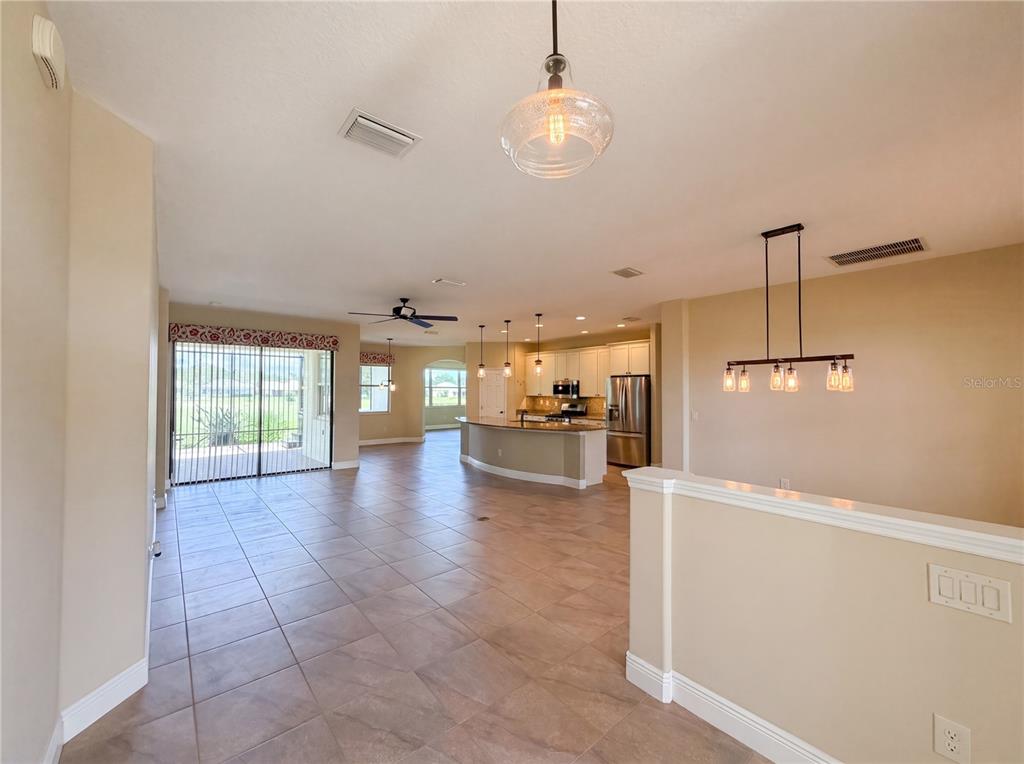 An open-concept kitchen and living area features tile flooring, a curved island, and pendant lighting — 27103 CAMERONS RUN, LEESBURG, FL