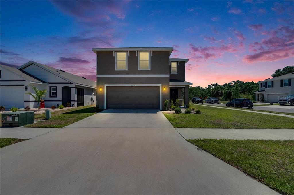 A two-story suburban house with a two-car garage and a concrete driveway at sunset — 16894 DELIA STREET, WIMAUMA, FL