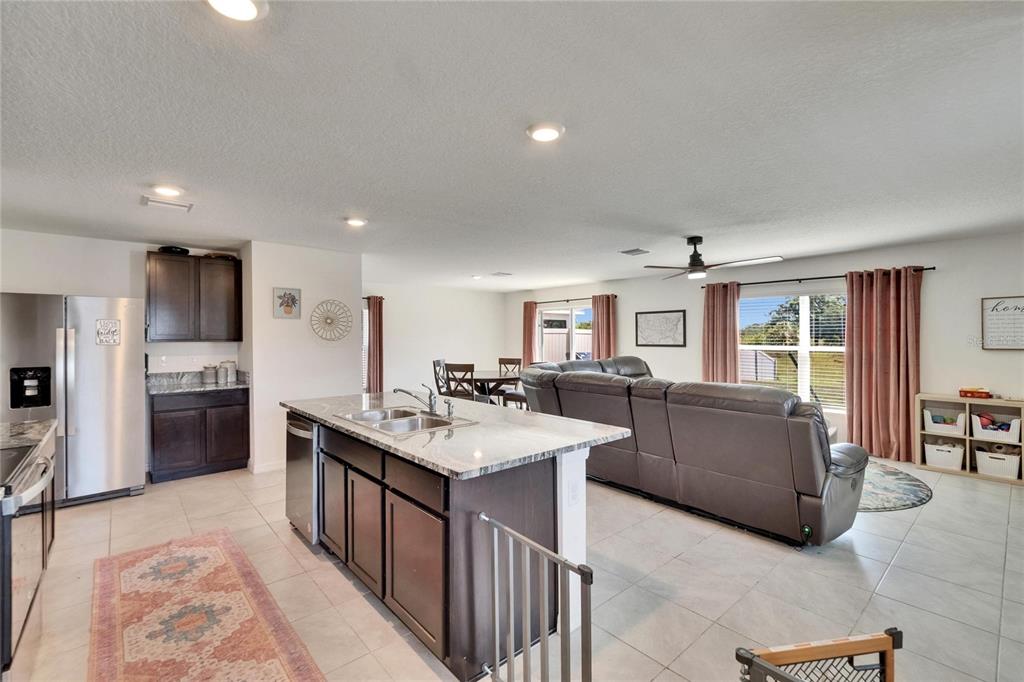 An open-concept kitchen with a granite island overlooks a living room and dining area — 16894 DELIA STREET, WIMAUMA, FL