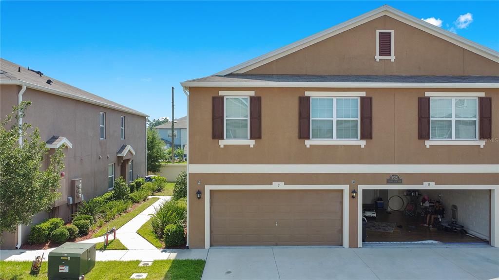 An exterior view of a two-story townhouse with a two-car garage and brown stucco siding — 3521 SENECA CLUB LOOP UNIT 103C, ORLANDO, FL